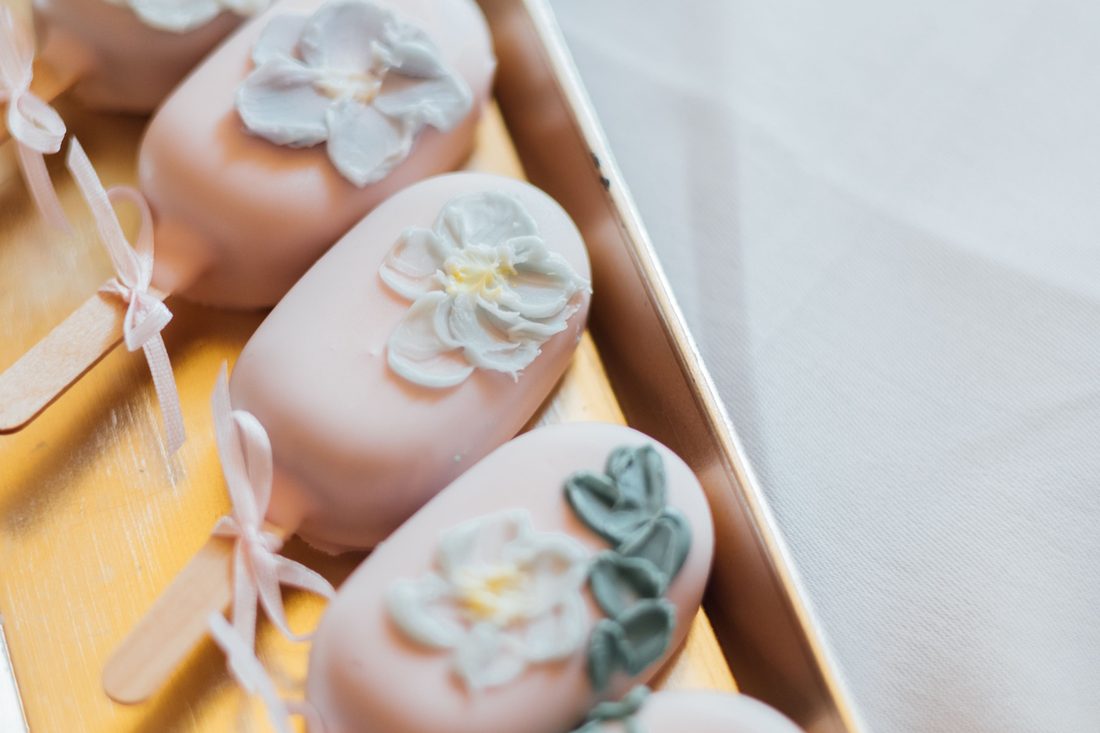 Blush cake pops with piped sugar flowers in a gold tray.