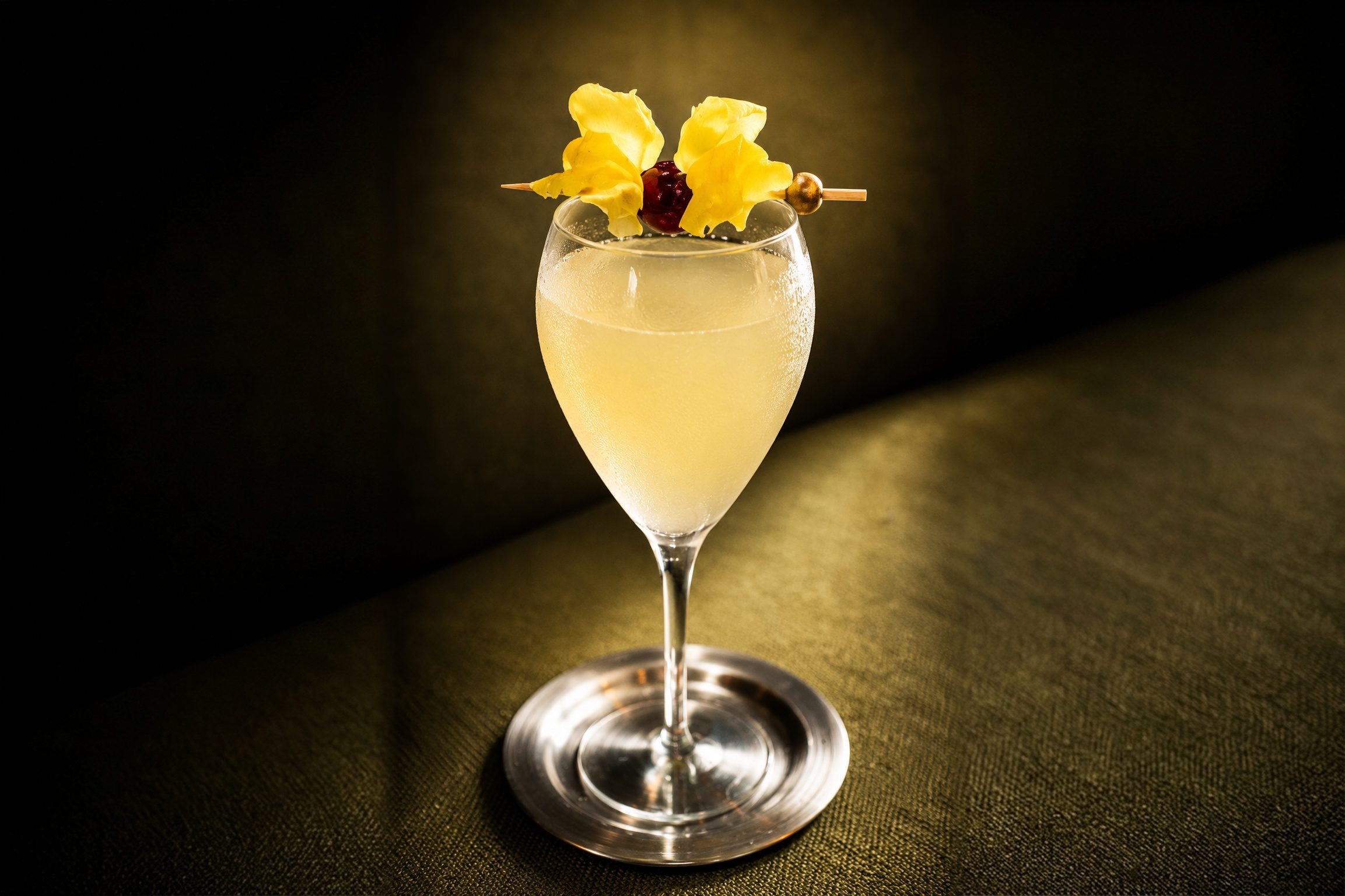 A French 25 cocktail in a stemmed glass, garnished with yellow flowers.