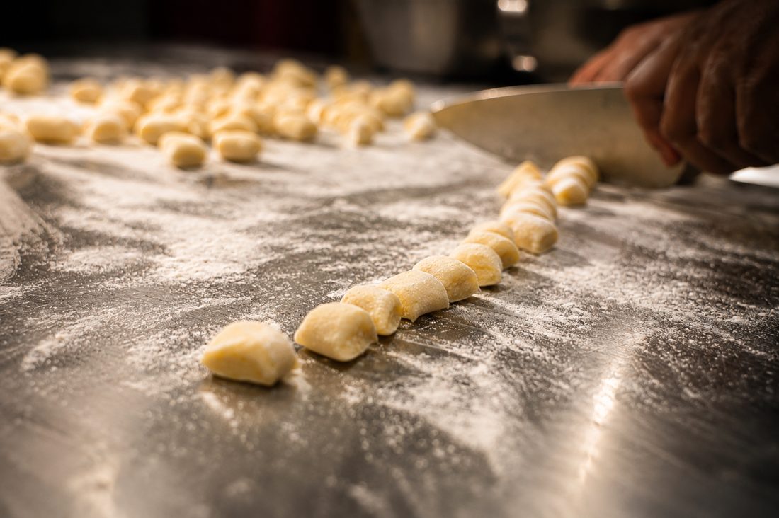 Hand-rolled gnocchi being cut on a floured counter.