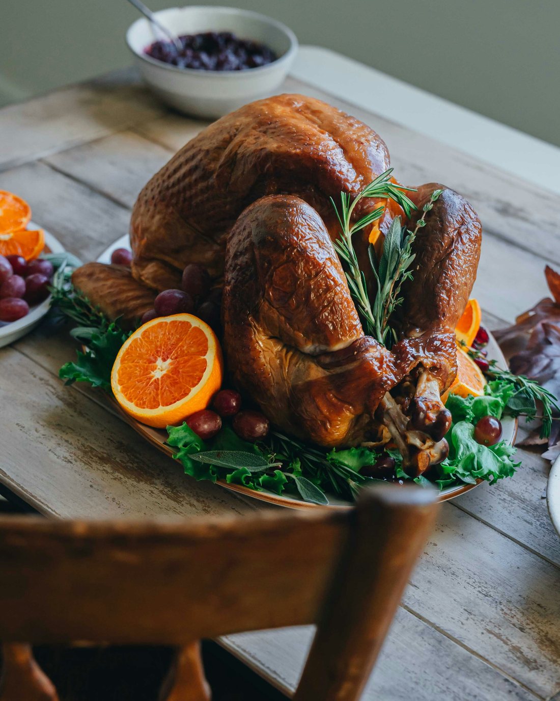 A whole roast turkey on a platter with orange halves, grapes and rosemary