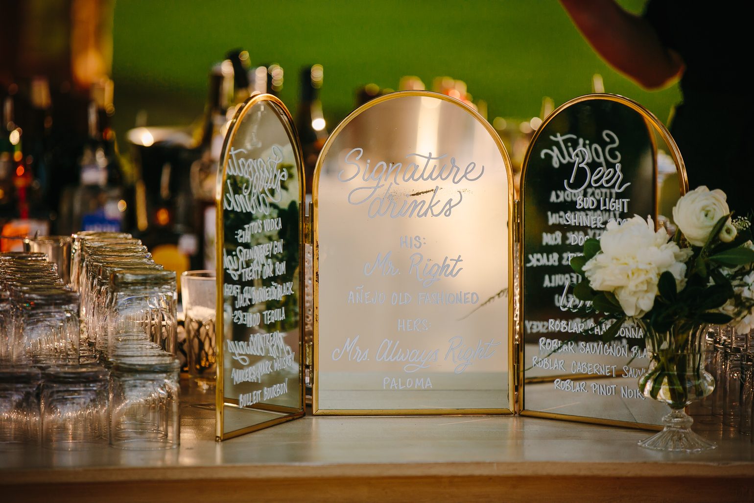 A gold-framed signature drinks menu on the bar at a wedding: his, Mr. Right, an añejo old fashioned; hers, Mrs. Always Right, a paloma.